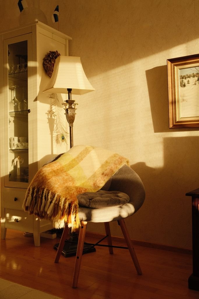 Warmly lit cozy corner with a chair, blanket, and lamp. Perfect for relaxation.